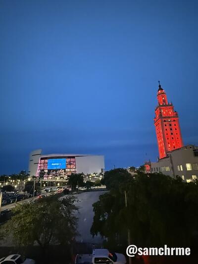 Kaseya Center ao entardecer, ao lado de uma torre de tijolos iluminada de vermelho