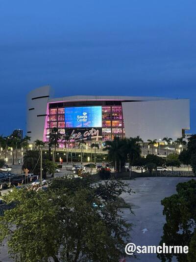 Kaseya Center à noite, com a fachada iluminada em rosa e um telão azul