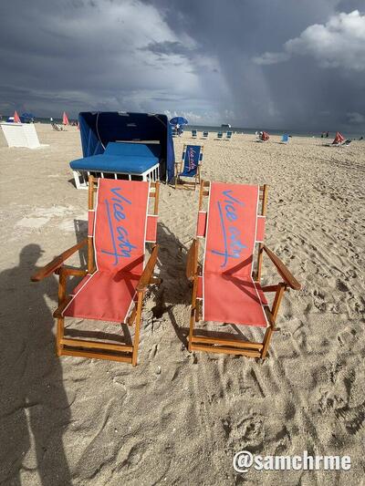 Cadeiras vermelhas "Vice City" diante de uma cabana azul, com tempestade ao longe
