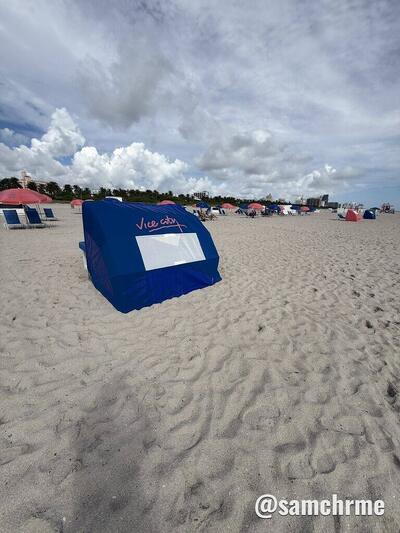 Cabana azul com "Vice City" escrito e uma janela branca, na areia da praia