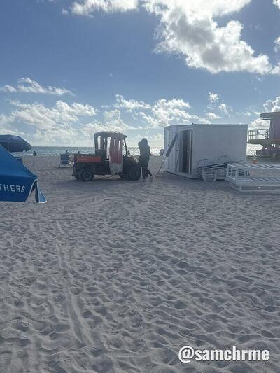Veículo utilitário vermelho e cabine branca de apoio, na areia da praia