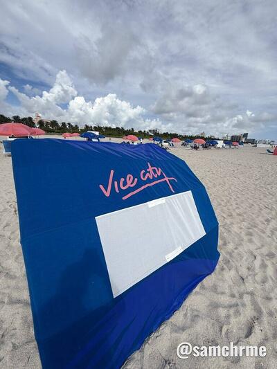 Lona azul com "Vice City" em rosa e um espaço branco, esticada na areia