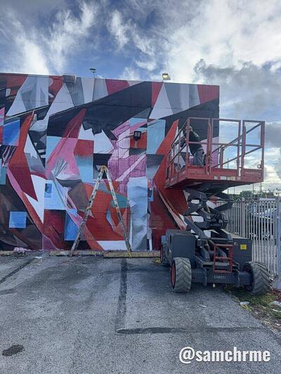 Plataforma elevatória diante do mural em construção, com formas geométricas vermelhas, rosas e azuis
