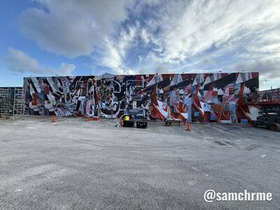 O mural abstrato no muro, com cones laranja no estacionamento à frente