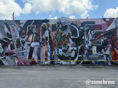 Detalhe do mural em formas geométricas pretas, vermelhas, rosas e azuis, com fita amarela de isolamento