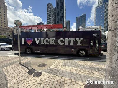 Ônibus "I ♥ Vice City" visto de lado, com o teto aberto e prédios altos ao fundo
