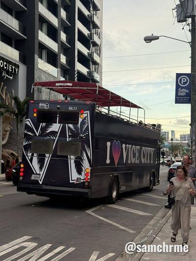 Ônibus "I ♥ Vice City" com palmeiras brancas e roxas na traseira, numa rua do centro com pedestres