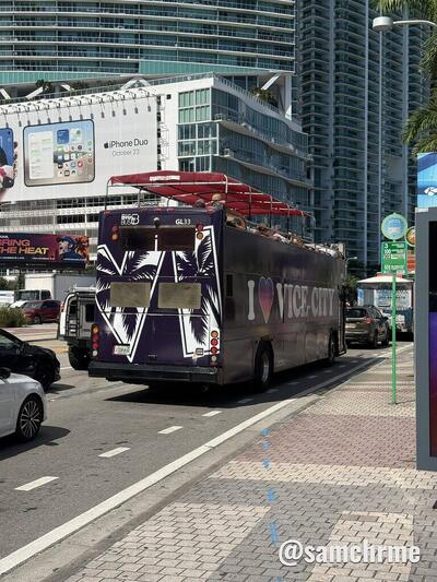 Traseira do ônibus "I ♥ Vice City" com as palmeiras estampadas, parado numa rua com prédios ao fundo